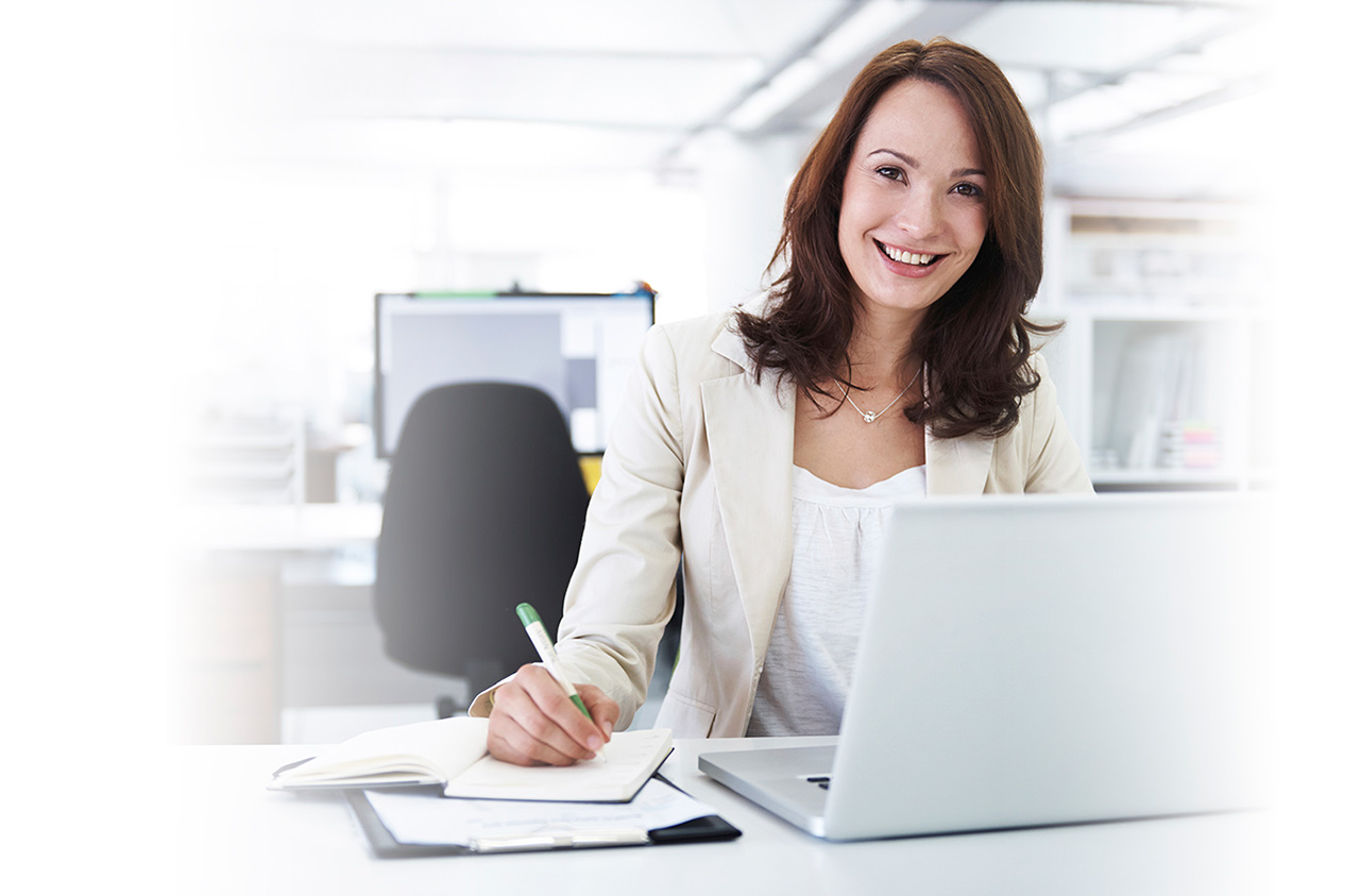 Portrait of a beautiful young businesswoman writing notes in a notebook while using her laptop