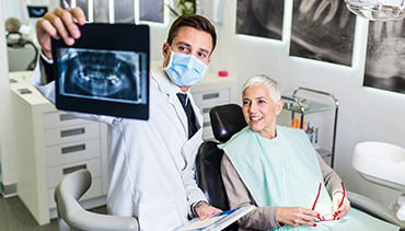940518764 Handsome male dentist checking x-ray image or scan while beautiful senior woman receiving a dental treatment.